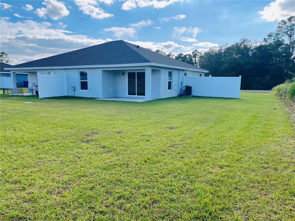 The back exterior of a single-story house features a concrete patio and white vinyl fencing — 6917 SAN BENITO DRIVE, SEBRING, FL