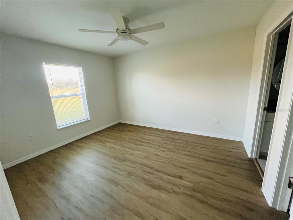 An empty bedroom features light-colored walls, wood-look flooring, a ceiling fan, and a window — 6917 SAN BENITO DRIVE, SEBRING, FL