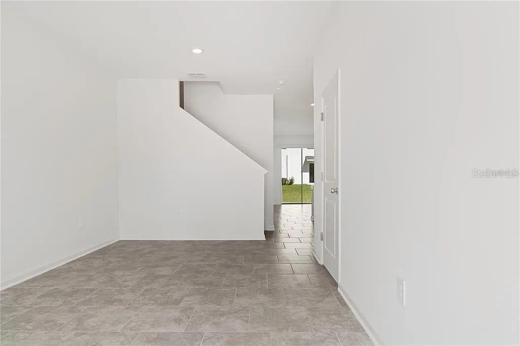 A room with gray tile flooring features a white staircase and a closed door — 3334 LAURENT LOOP, DAVENPORT, FL