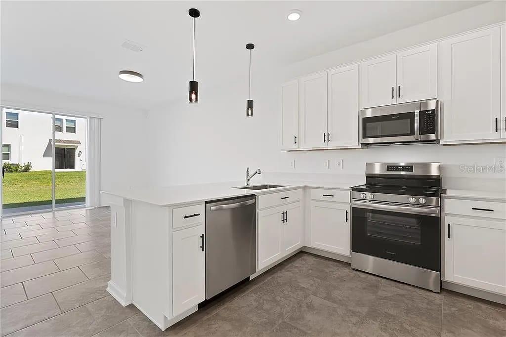 A modern kitchen features white cabinets, stainless steel appliances, and a peninsula with pendant lighting — 3334 LAURENT LOOP, DAVENPORT, FL