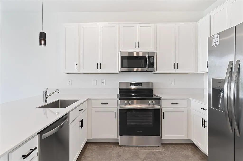 A modern kitchen features white cabinets, stainless steel appliances, and light-colored countertops — 3334 LAURENT LOOP, DAVENPORT, FL