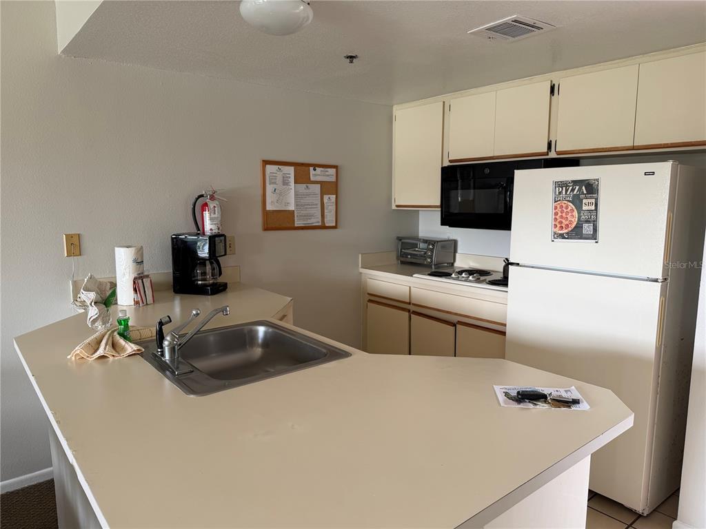A kitchen features white cabinets, a white refrigerator, a stainless steel sink, and beige countertops — 6324 PARC CORNICHE DRIVE UNIT 1202, ORLANDO, FL