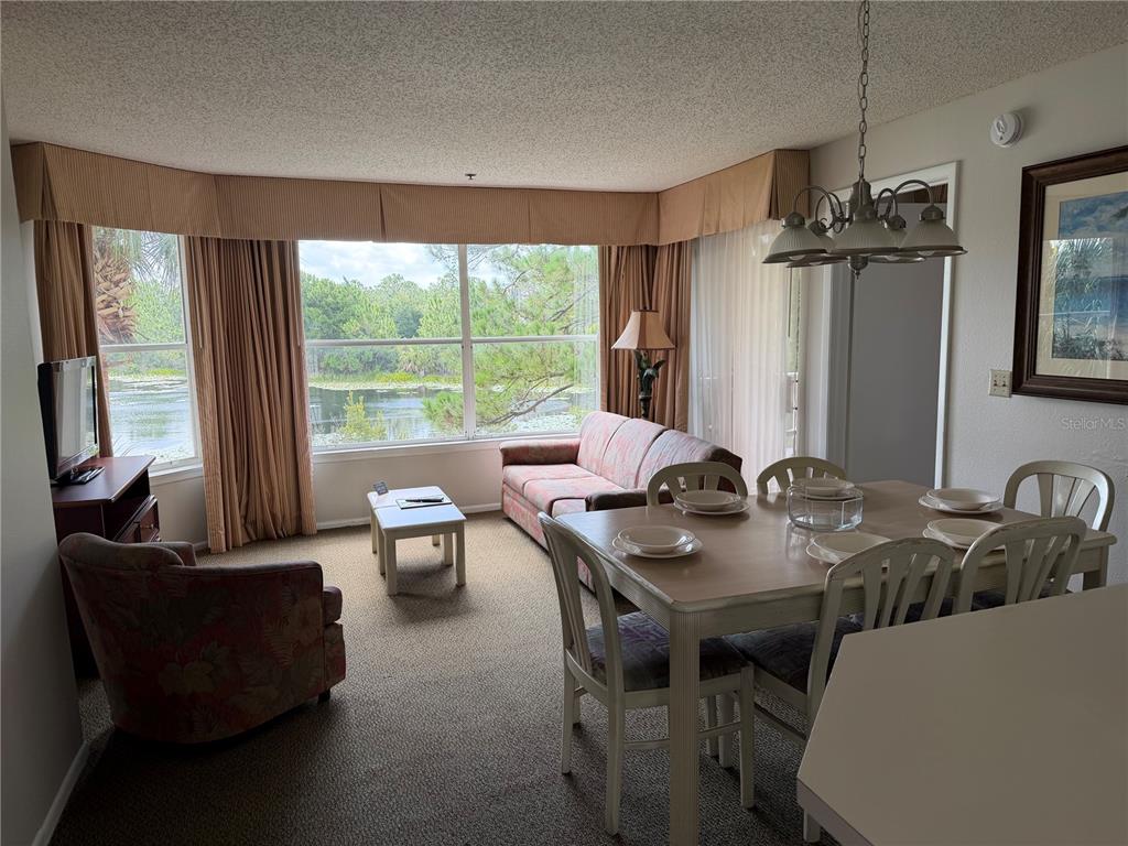 A living and dining area features carpeted floors, a sofa, a dining table, and lake views — 6324 PARC CORNICHE DRIVE UNIT 1202, ORLANDO, FL