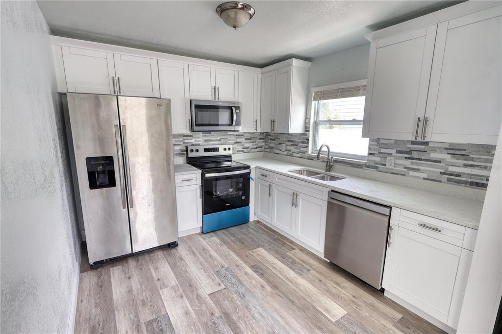 A kitchen features white cabinets, stainless steel appliances, a tiled backsplash, and wood-look flooring — 116 44TH STREET S, ST PETERSBURG, FL