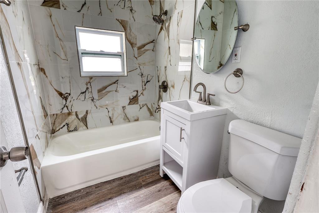 A bathroom features a white vanity, a toilet, and a bathtub with marble-patterned tile walls — 116 44TH STREET S, ST PETERSBURG, FL