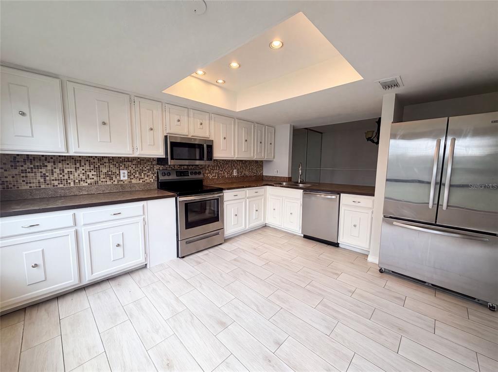 A kitchen with white cabinets, stainless steel appliances, a mosaic backsplash, and light wood-look flooring — 4747 PURITAN CIRCLE UNIT 523, TAMPA, FL