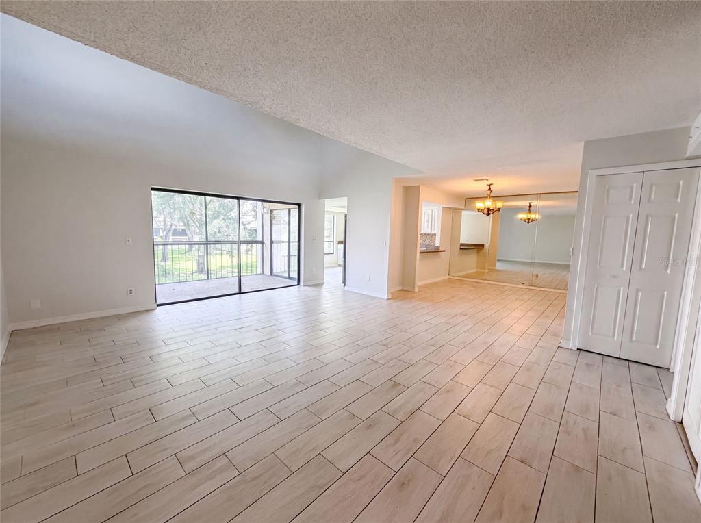 An open-concept living area features light wood-look tile flooring, vaulted ceilings, and a sliding glass door — 4747 PURITAN CIRCLE UNIT 523, TAMPA, FL