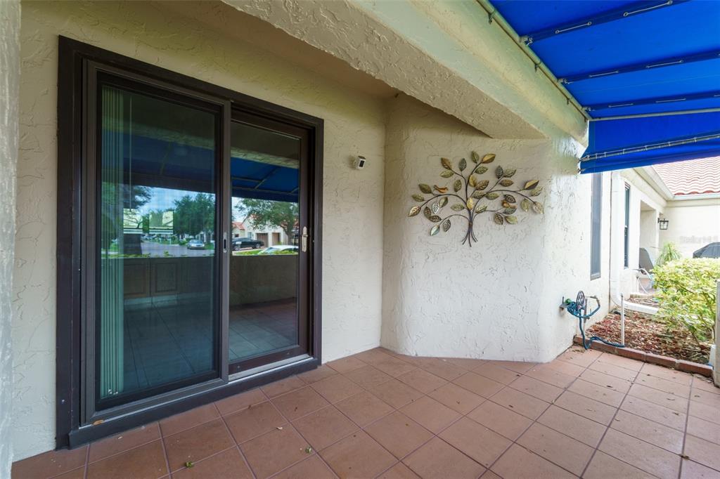 A covered patio features tiled flooring, a sliding glass door, and a metal tree wall decoration — 4002 87TH TERRACE N, PINELLAS PARK, FL