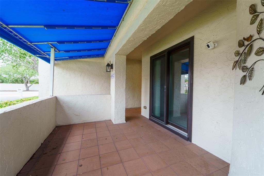 A covered patio features tiled flooring, a blue awning, and a sliding glass door — 4002 87TH TERRACE N, PINELLAS PARK, FL