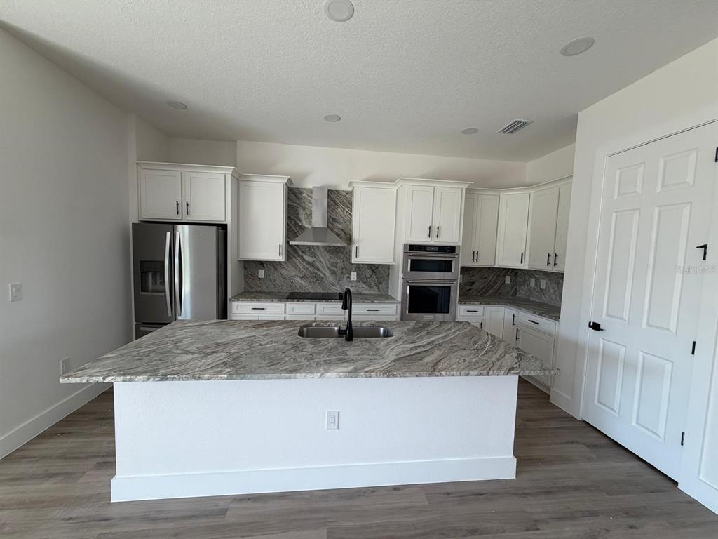 A kitchen features white cabinets, a large granite island, stainless steel appliances, and wood flooring — 13 LATEEN SAIL DRIVE, PLACIDA, FL