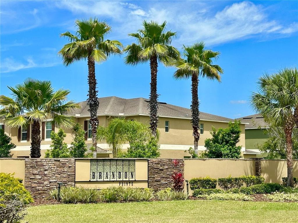 A stone wall with a Brandon Pointe sign sits in front of palm trees and houses — 1607 ACADIA HARBOR PLACE, BRANDON, FL