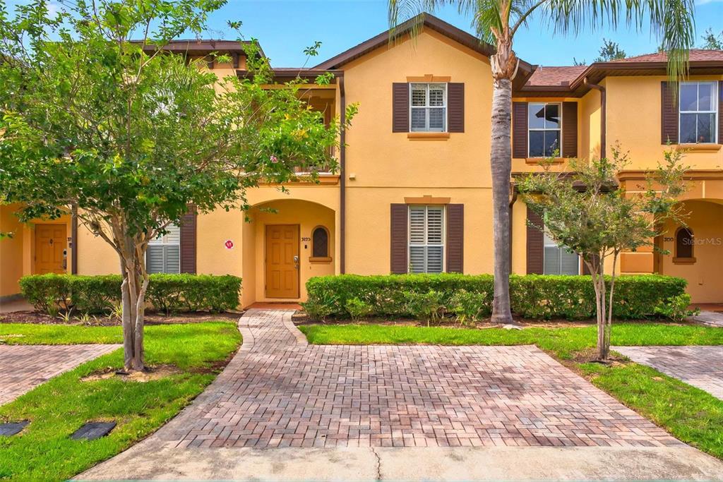 A two-story yellow townhouse with a paved driveway, a front porch, and brown shutters — 3725 CALABRIA AVENUE, DAVENPORT, FL