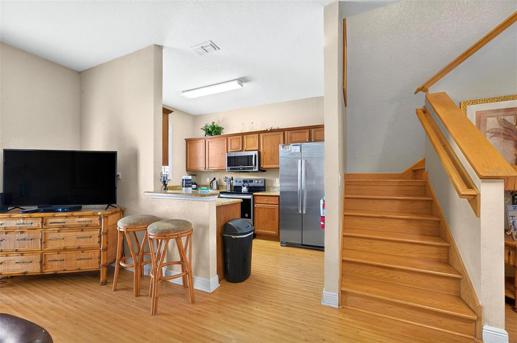 A kitchen with wood cabinets and stainless steel appliances sits beside a staircase and television — 3725 CALABRIA AVENUE, DAVENPORT, FL