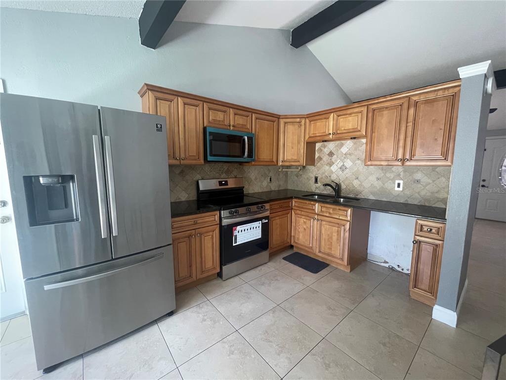 A kitchen features wood cabinets, stainless steel appliances, dark countertops, and a tiled backsplash — 8524 CATALINA DRIVE, TAMPA, FL