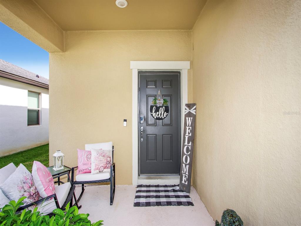 A covered front porch features a dark gray door, a welcome sign, and patio furniture — 1833 CAYMAN COVE CIRCLE, ST CLOUD, FL