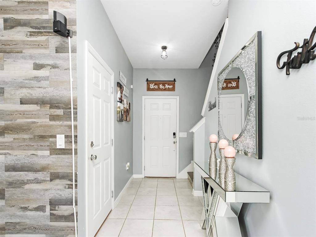 A tiled entryway features a wood-look accent wall, a mirrored console table, and a front door — 1833 CAYMAN COVE CIRCLE, ST CLOUD, FL