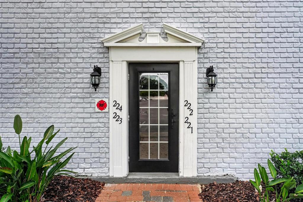 A black glass-paneled door with white trim is centered on a light gray brick wall — 222 LEWFIELD CIRCLE, WINTER PARK, FL
