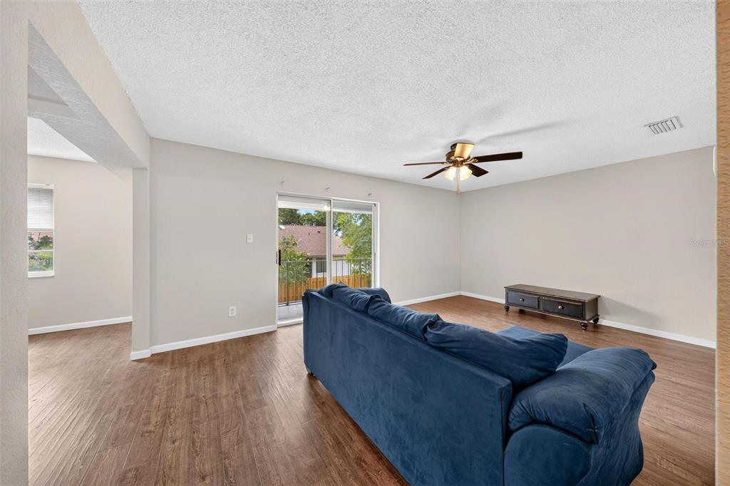 A living room with wood-look flooring, a blue sofa, a ceiling fan, and sliding glass doors — 222 LEWFIELD CIRCLE, WINTER PARK, FL