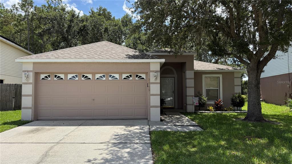 A single-story house with a tan stucco exterior, a two-car garage, and a large tree — 3242 ERSKINE DRIVE, ORLANDO, FL