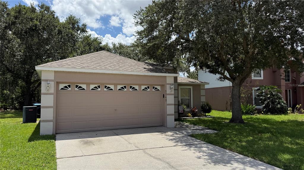 A beige house exterior features a two-car garage, a concrete driveway, and mature shade trees — 3242 ERSKINE DRIVE, ORLANDO, FL