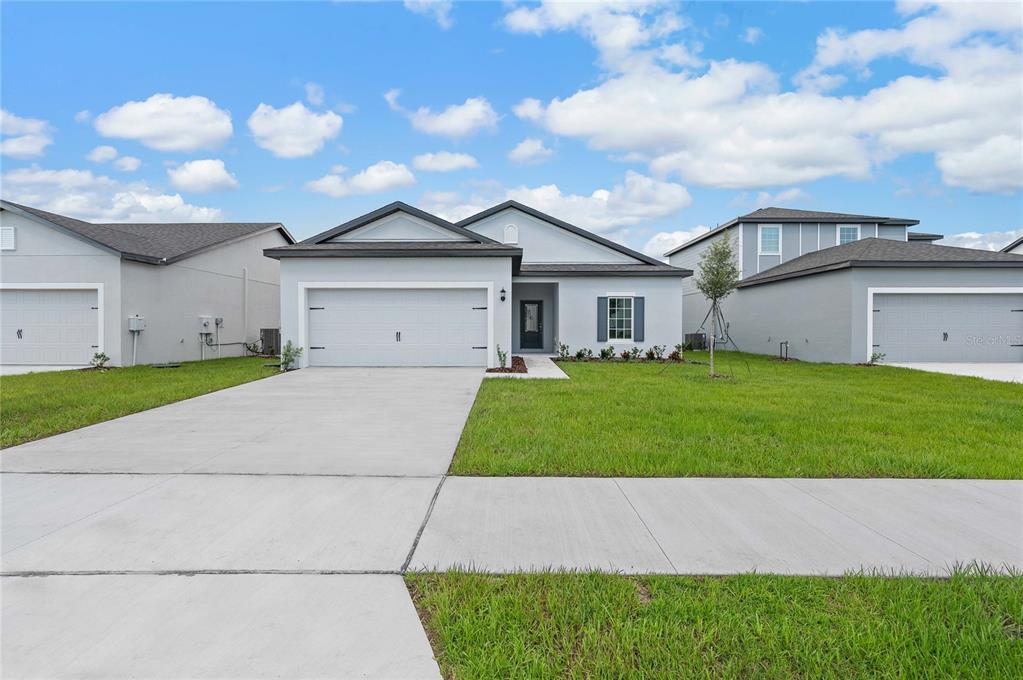 A single-story suburban house with a two-car garage, gray stucco exterior, and a concrete driveway — 13284 TULA LOOP, ASTATULA, FL