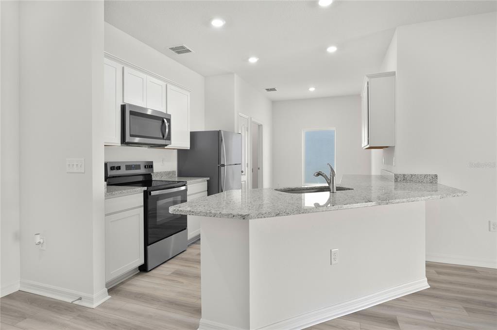 A kitchen with white cabinets, granite countertops, stainless steel appliances, and light wood-look flooring — 13284 TULA LOOP, ASTATULA, FL