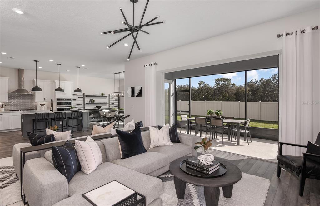 A modern living room with a sectional sofa opens to a covered patio and backyard — 5611 SYMPHONY SPRINGS TERRACE, PARRISH, FL