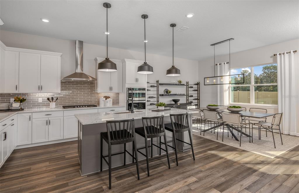 A modern kitchen features white cabinets, a gray island with bar stools, and an adjacent dining area — 5611 SYMPHONY SPRINGS TERRACE, PARRISH, FL