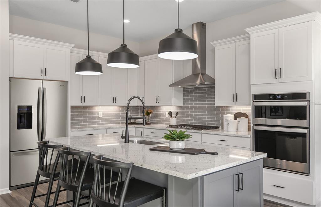 A modern kitchen features white cabinets, a gray tiled backsplash, stainless steel appliances, and an island — 5611 SYMPHONY SPRINGS TERRACE, PARRISH, FL