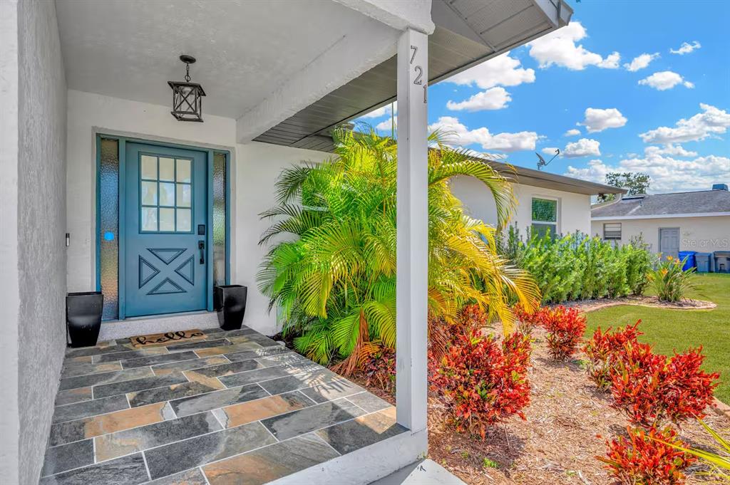 A blue front door with a glass pane sits under a covered porch with slate-tiled flooring — 721 EAGLE LANE, APOLLO BEACH, FL