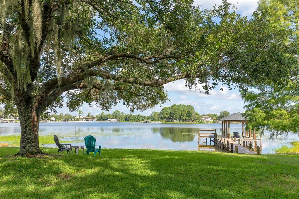 A grassy lawn with two chairs sits under a large tree overlooking a lake — 284 EVANSDALE ROAD, LAKE MARY, FL