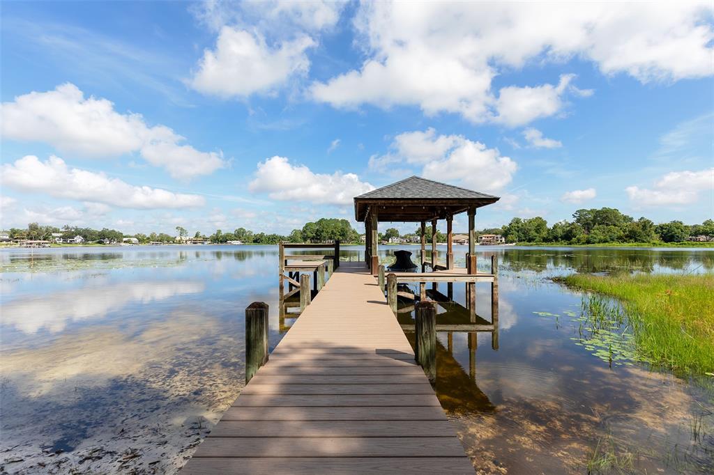 A wooden dock with a covered boat slip extends into a calm lake — 284 EVANSDALE ROAD, LAKE MARY, FL