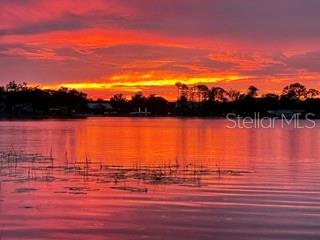 A vibrant sunset glows over a calm lake with silhouetted trees along the distant shoreline — 284 EVANSDALE ROAD, LAKE MARY, FL
