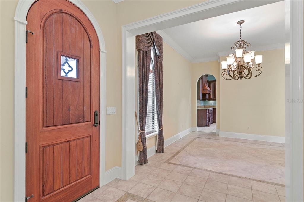 An entryway features a wooden arched door, tile flooring, and a chandelier in the dining area — 1421 CHAPMAN CIRCLE, WINTER PARK, FL