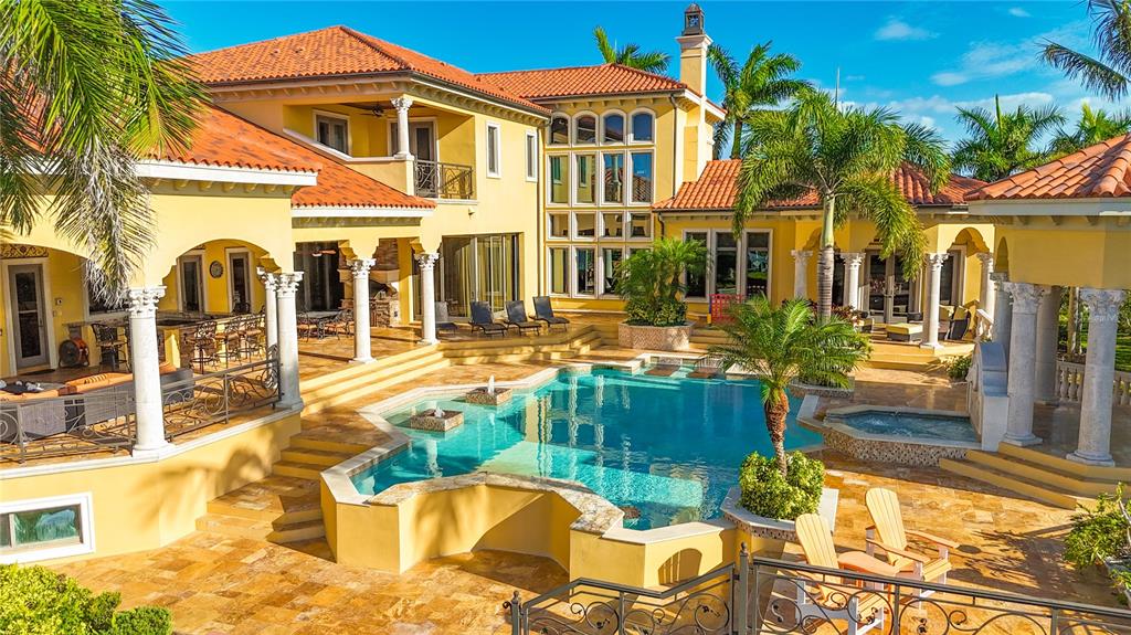 A yellow Mediterranean-style house features a large swimming pool, stone patio, and palm trees — 1363 OCEANVIEW DRIVE, TIERRA VERDE, FL