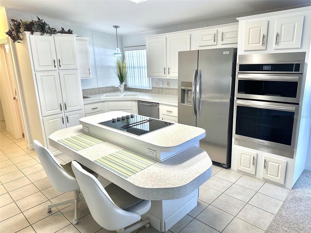 A kitchen features white cabinetry, a center island with a cooktop, and stainless steel appliances — 11244 101ST WAY UNIT 136, LARGO, FL