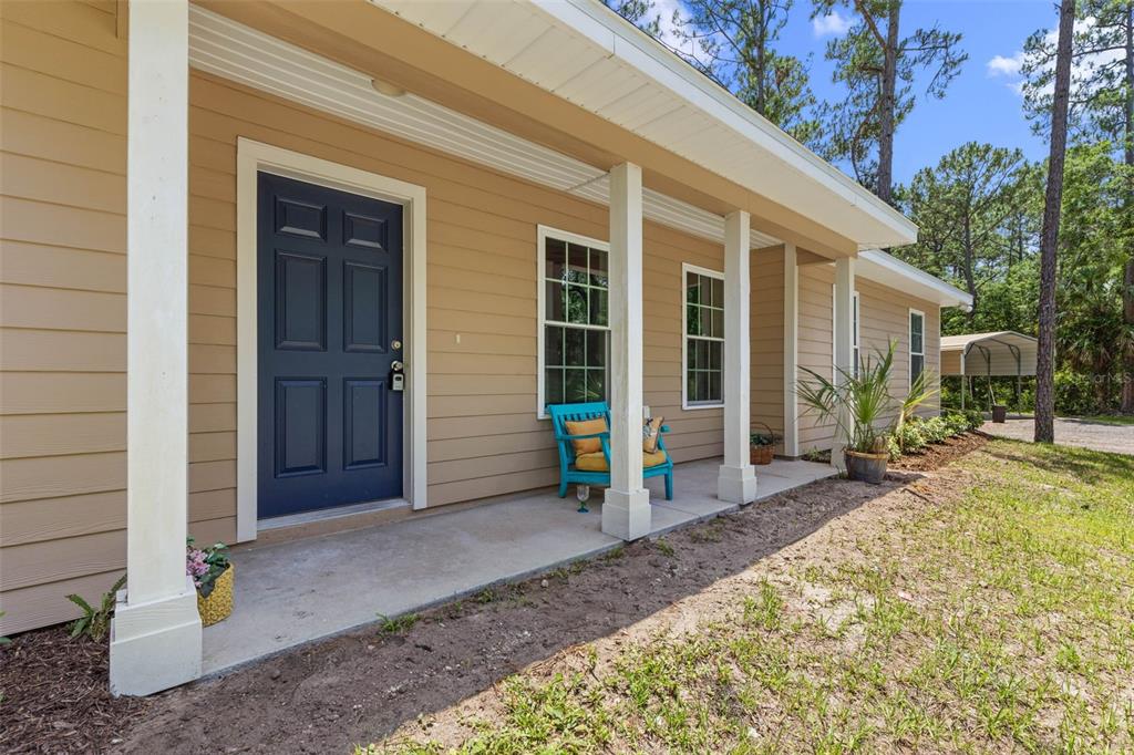A tan house and a large metal carport sit on a gravel lot among trees — 3296 N OLD DIXIE HIGHWAY, BUNNELL, FL