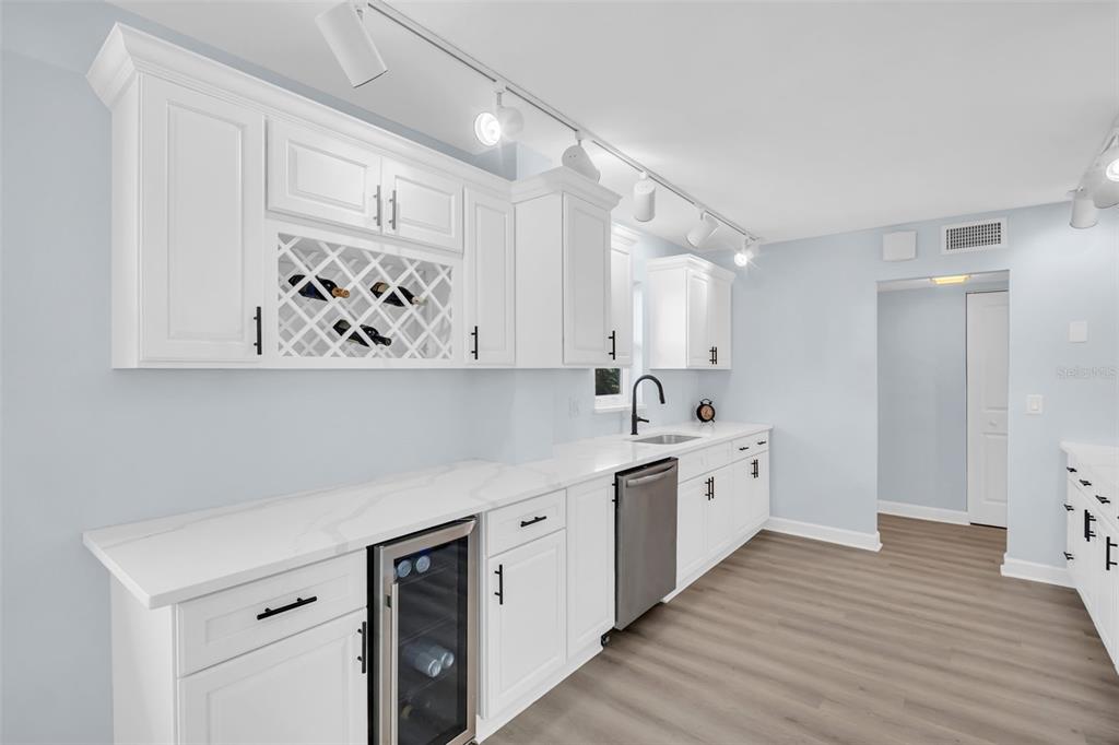 A white kitchen features a wine cooler, a stainless steel dishwasher, and a wine rack — 7930 SUN ISLAND DRIVE S UNIT 104, SOUTH PASADENA, FL
