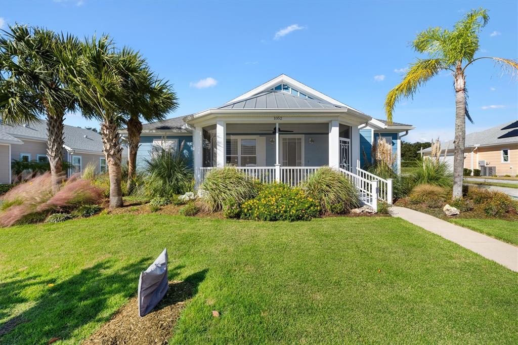 A blue house with a screened-in front porch, white railings, and palm trees in the yard — 1052 SUGAR LOAF KEY LOOP, LADY LAKE, FL