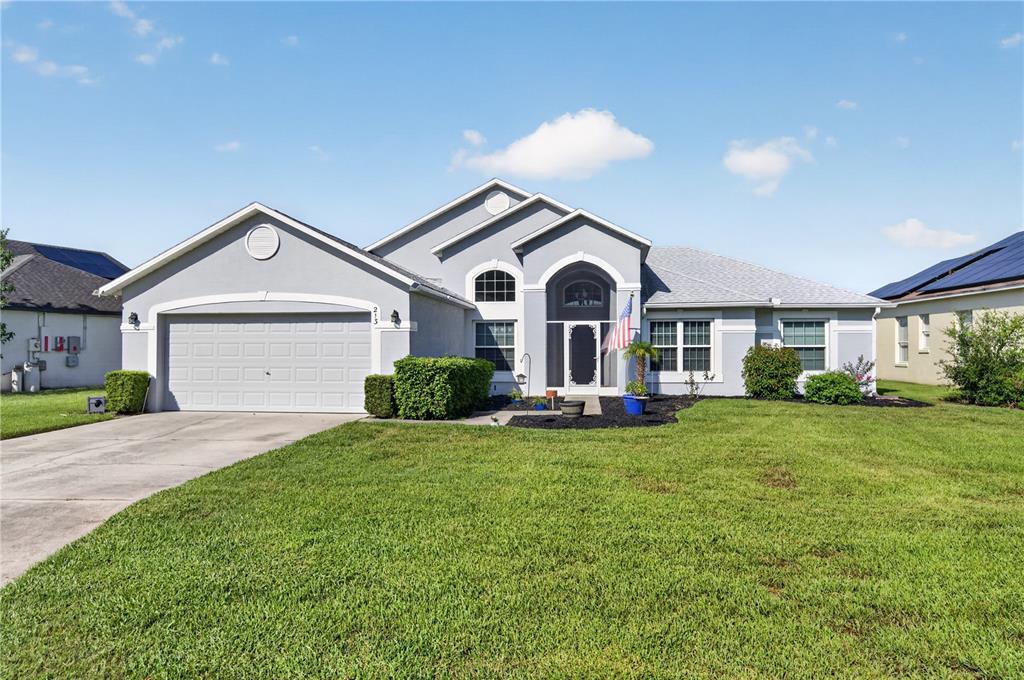 A single-story suburban house with a gray stucco exterior, a two-car garage, and a lawn — 213 SPANISH MOSS ROAD, DAVENPORT, FL