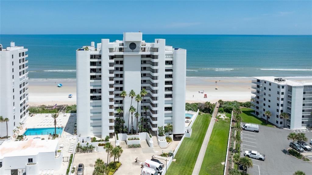An aerial view shows three white high-rise condominium buildings situated along a sandy beach — 5275 S ATLANTIC AVENUE UNIT 1007, NEW SMYRNA BEACH, FL