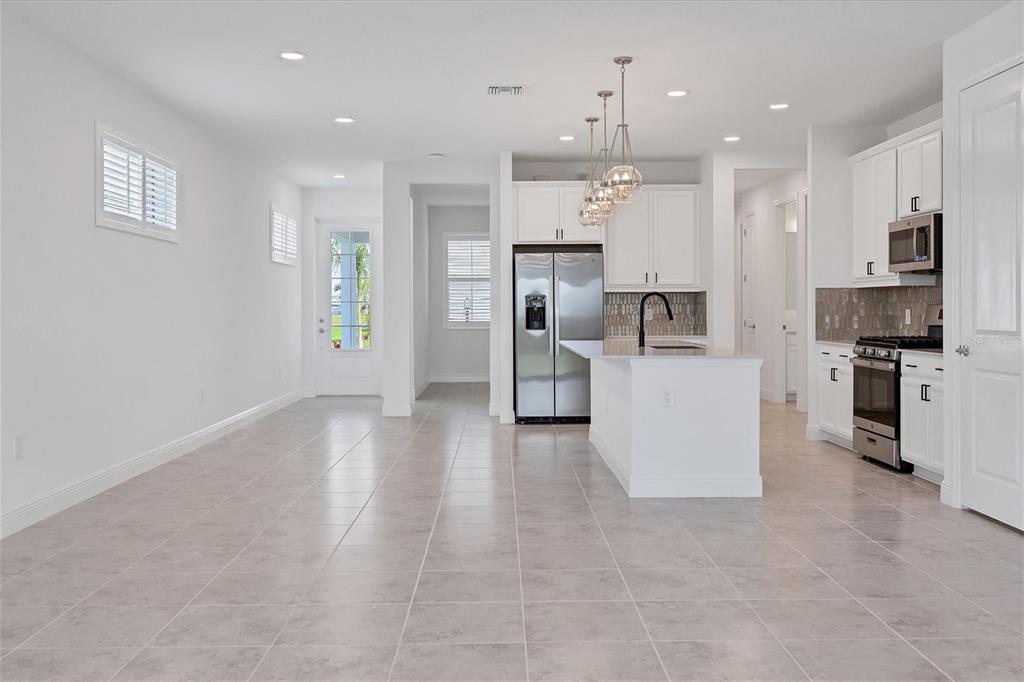 A bright, open-concept kitchen features white cabinetry, stainless steel appliances, and light-colored tile flooring — 8177 STERNWAY ROAD, SARASOTA, FL