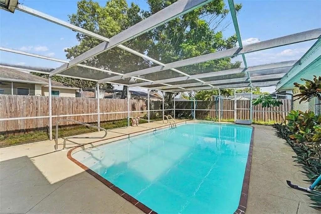 An outdoor swimming pool enclosed by a screened lanai with a concrete deck and fence — 11022 SALT TREE DRIVE, PORT RICHEY, FL