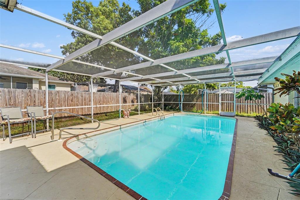 An outdoor swimming pool enclosed by a screened lanai with a concrete deck and fence — 11022 SALT TREE DRIVE, PORT RICHEY, FL
