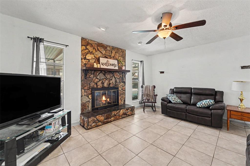 A living room features a stone fireplace, tile flooring, a ceiling fan, and a leather sofa — 11022 SALT TREE DRIVE, PORT RICHEY, FL