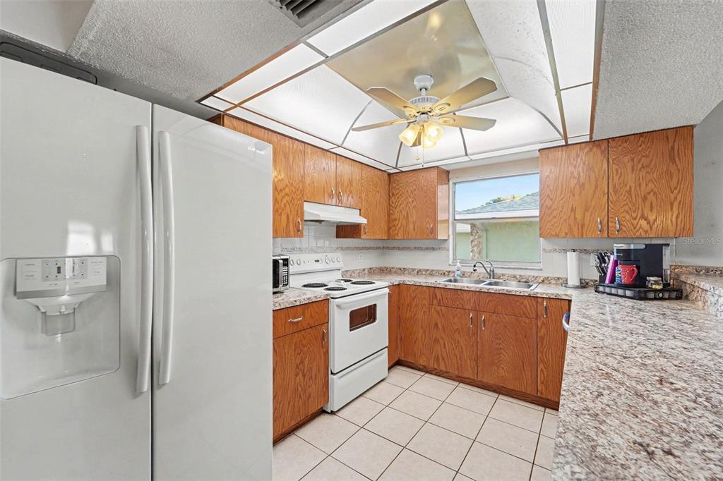 A kitchen features wood cabinets, white appliances, granite-look countertops, and a tray ceiling with lighting — 11022 SALT TREE DRIVE, PORT RICHEY, FL