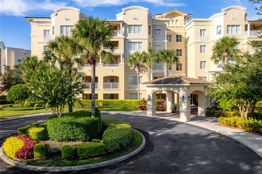A multi-story beige apartment building features a circular driveway and a covered entrance portico — 8495 MIRACLE DRIVE UNIT 206, CHAMPIONS GATE, FL