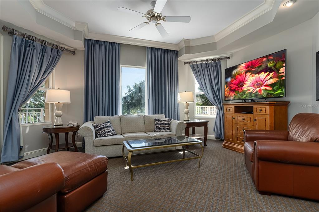A living room features a beige sofa, leather armchairs, a television, and blue floor-length curtains — 8495 MIRACLE DRIVE UNIT 206, CHAMPIONS GATE, FL