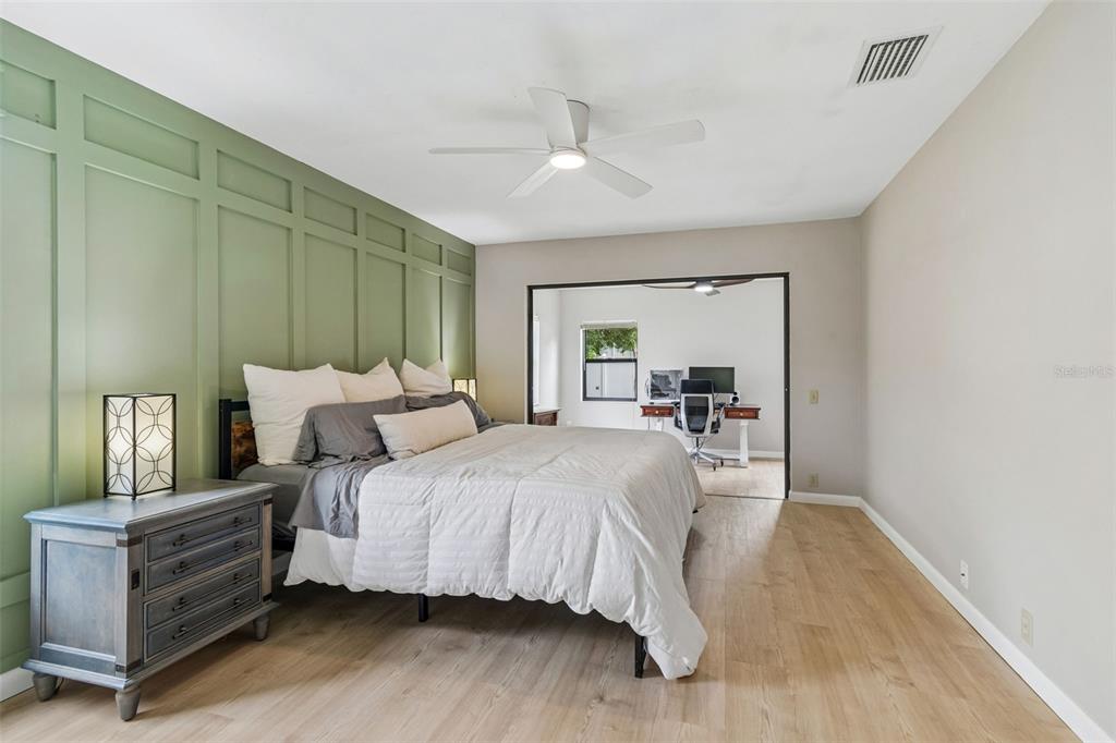 A bedroom features a green paneled accent wall, a bed, and an adjacent home office — 525 WALKER ROAD, SAFETY HARBOR, FL