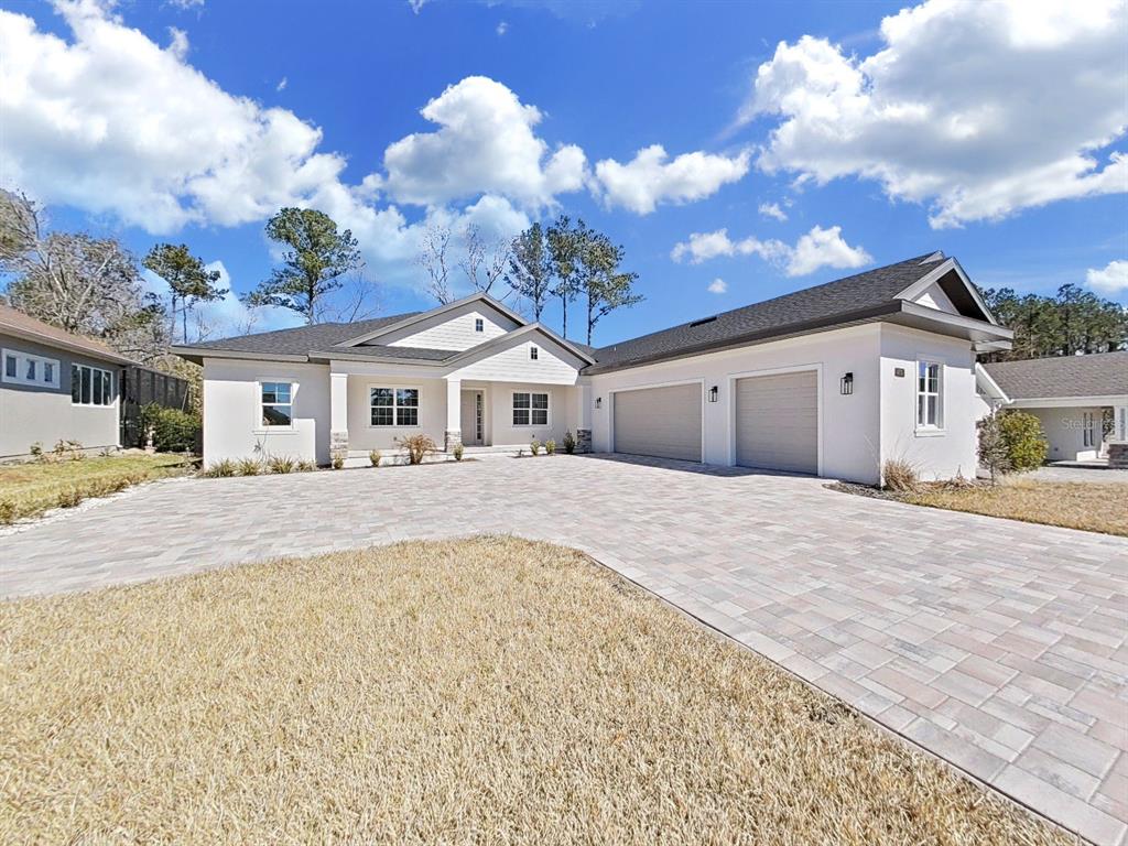 A single-story white house with a paved driveway and a two-car garage under a blue sky — 4716 HICKORY OAK DRIVE, BROOKSVILLE, FL